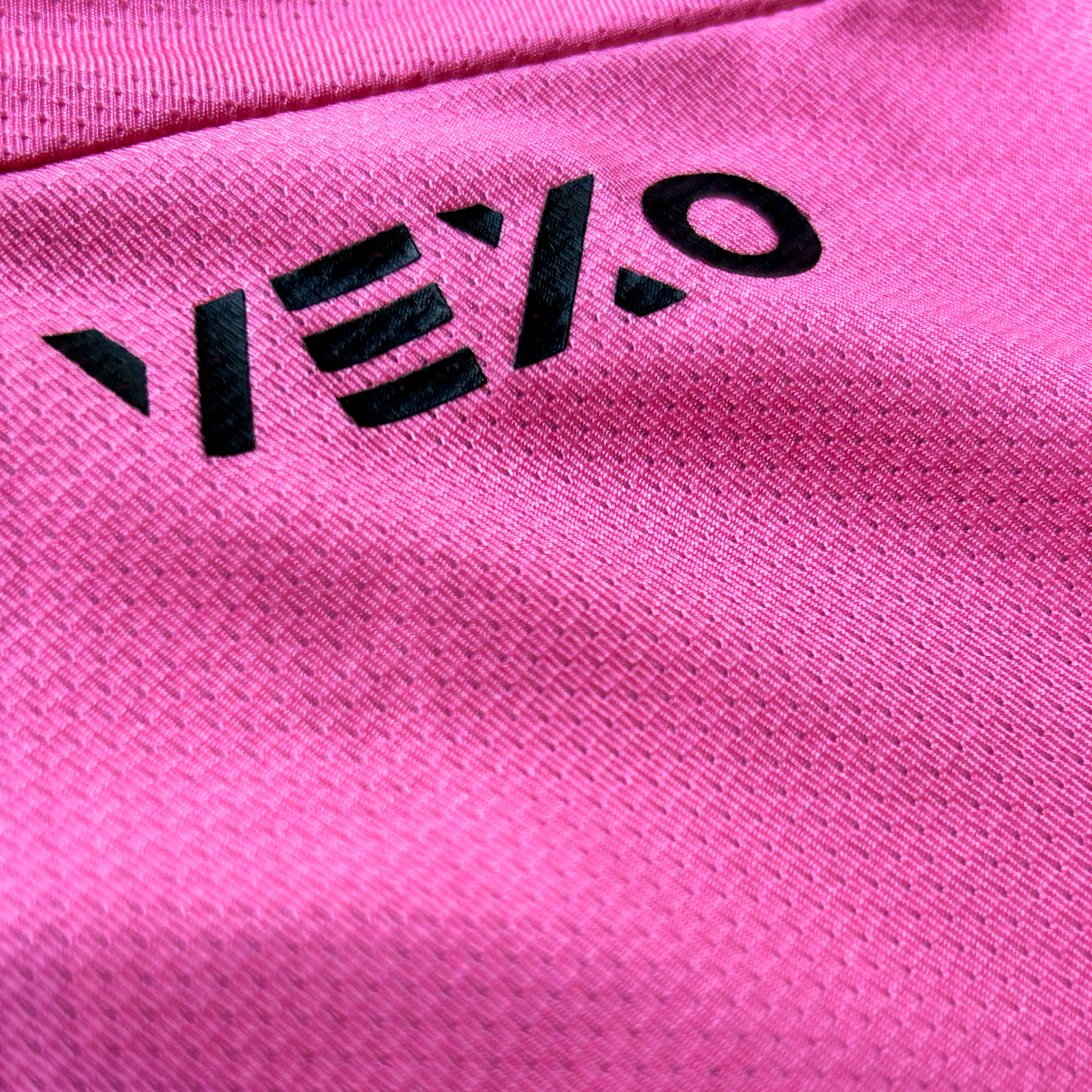 Close-up of a bright pink textured fabric with a black stylized Vexo logo printed vertically along the left side.