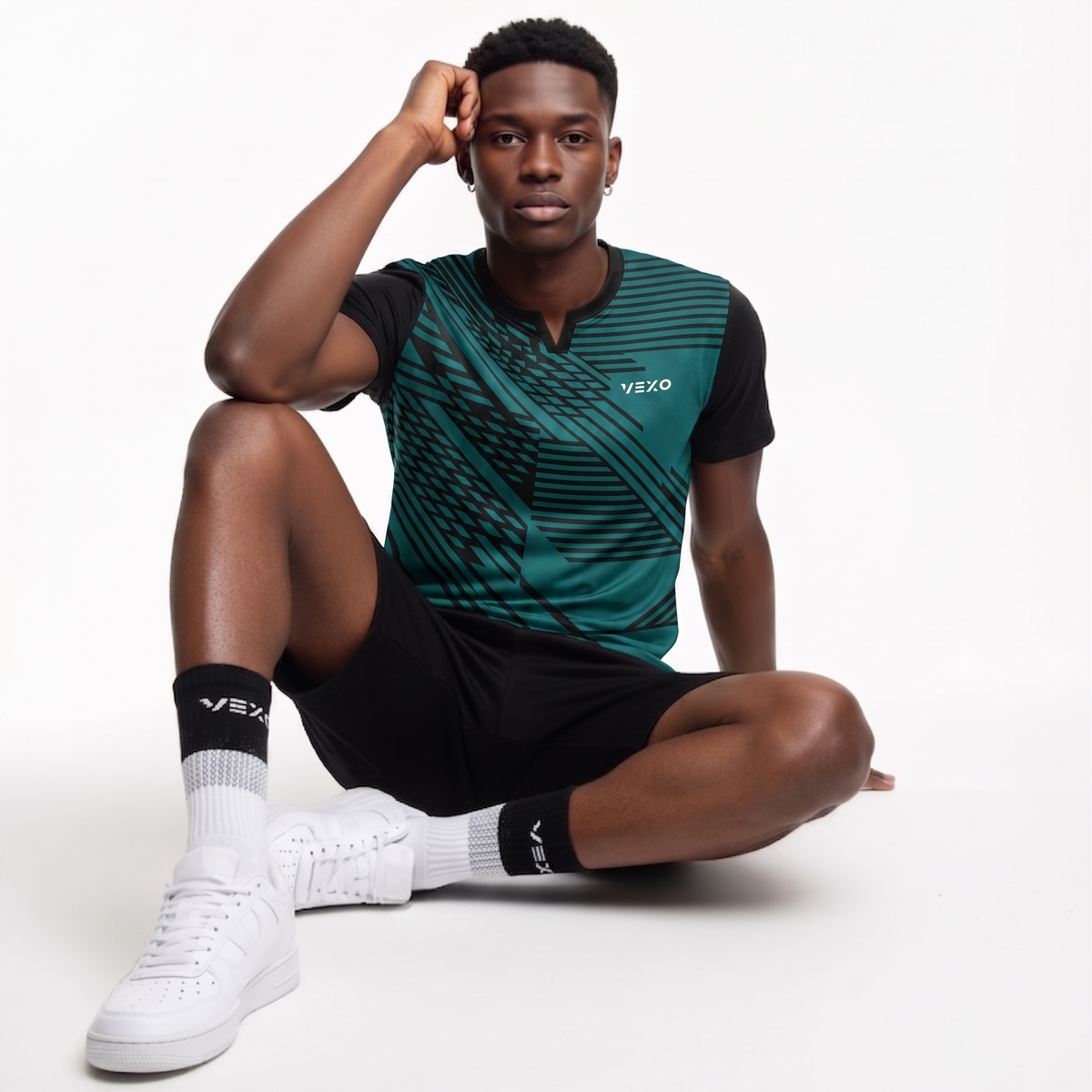 Model wearing VEXO athletic wear: teal geometric print t-shirt and black shorts. White sneakers & socks.