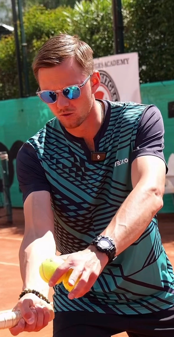 Tennis player with sunglasses on clay court holding two yellow balls and racket.