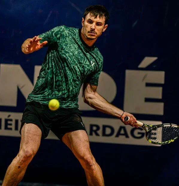 Tennis player in green shirt hitting ball on court with large blue banner in background