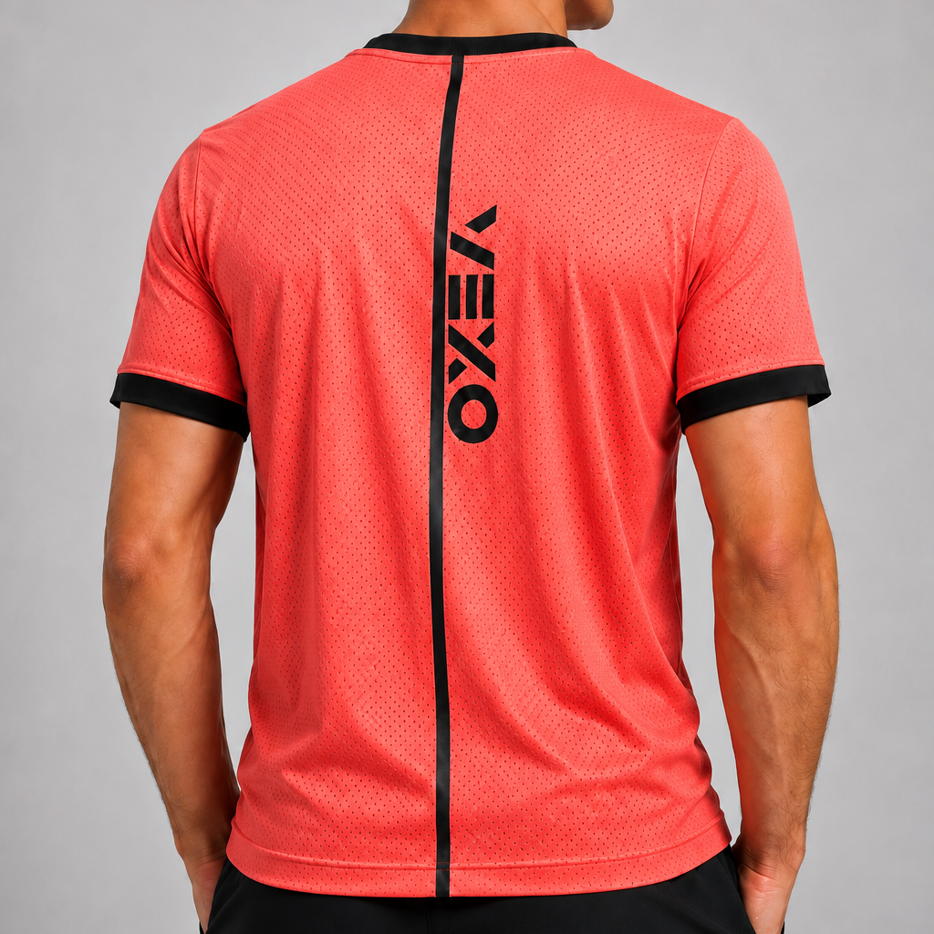 A man viewed from the back wearing a coral red athletic t-shirt with black trim and a vertical black VEXO logo on the back, paired with black shorts against a gray studio background.